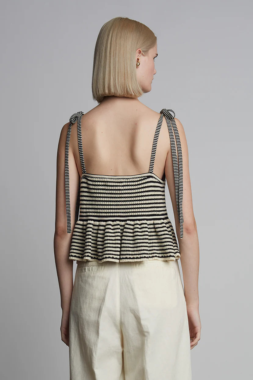 Woman wearing a black and white striped top with thin straps on a gray background