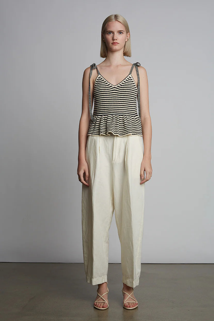 Woman wearing a striped tank top and white pants against a plain background