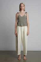Woman wearing a striped tank top and white pants against a plain background