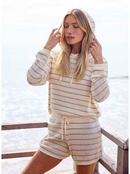 Woman wearing a crochet hoodie and shorts set by the sea.