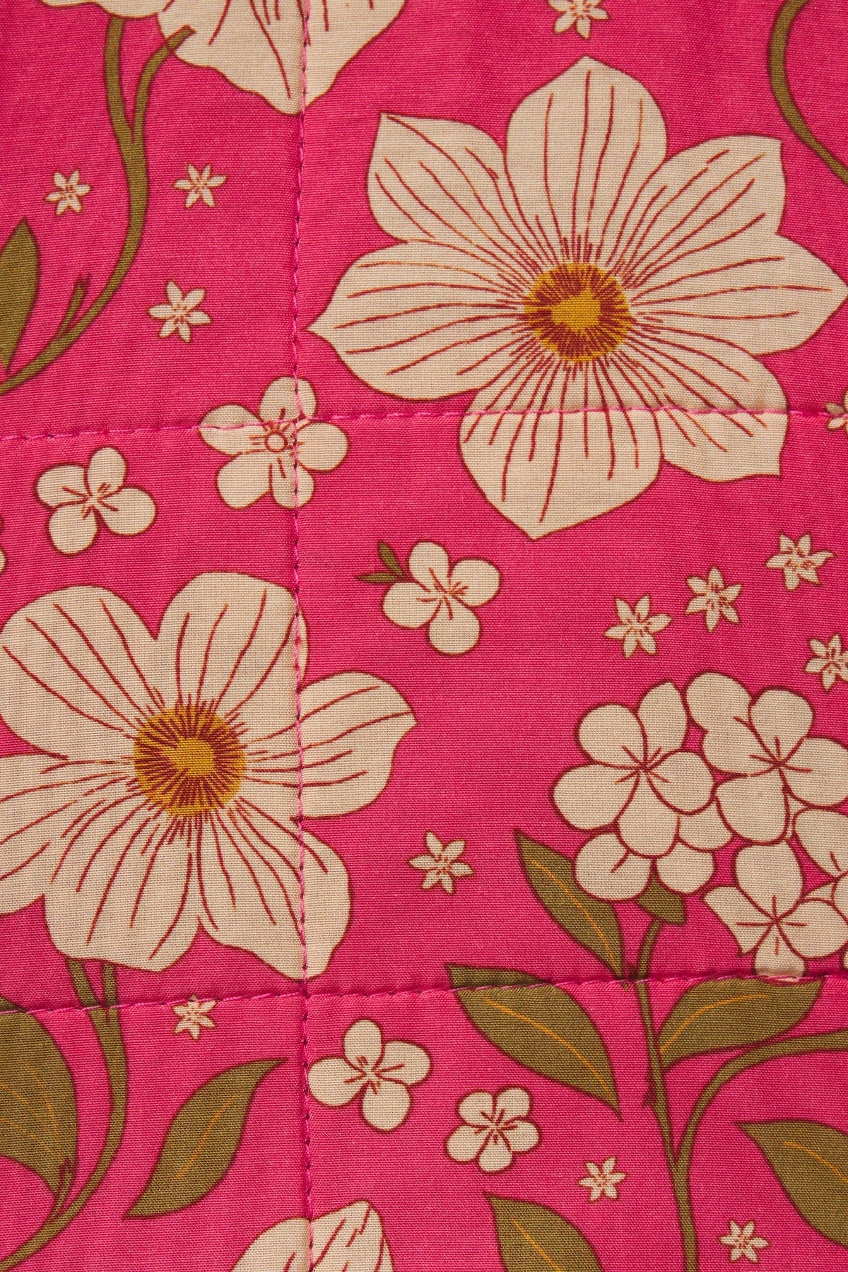 A close-up of a quilted fabric featuring a vibrant pink background with large cream-colored flowers, olive green leaves, and small white blossoms.