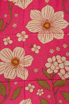 A close-up of a quilted fabric featuring a vibrant pink background with large cream-colored flowers, olive green leaves, and small white blossoms.