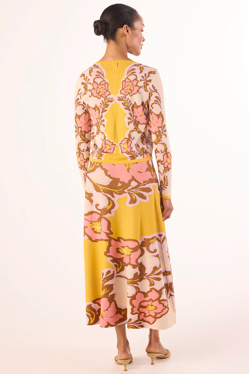 Woman wearing a floral dress with a yellow top and pink skirt on a white background