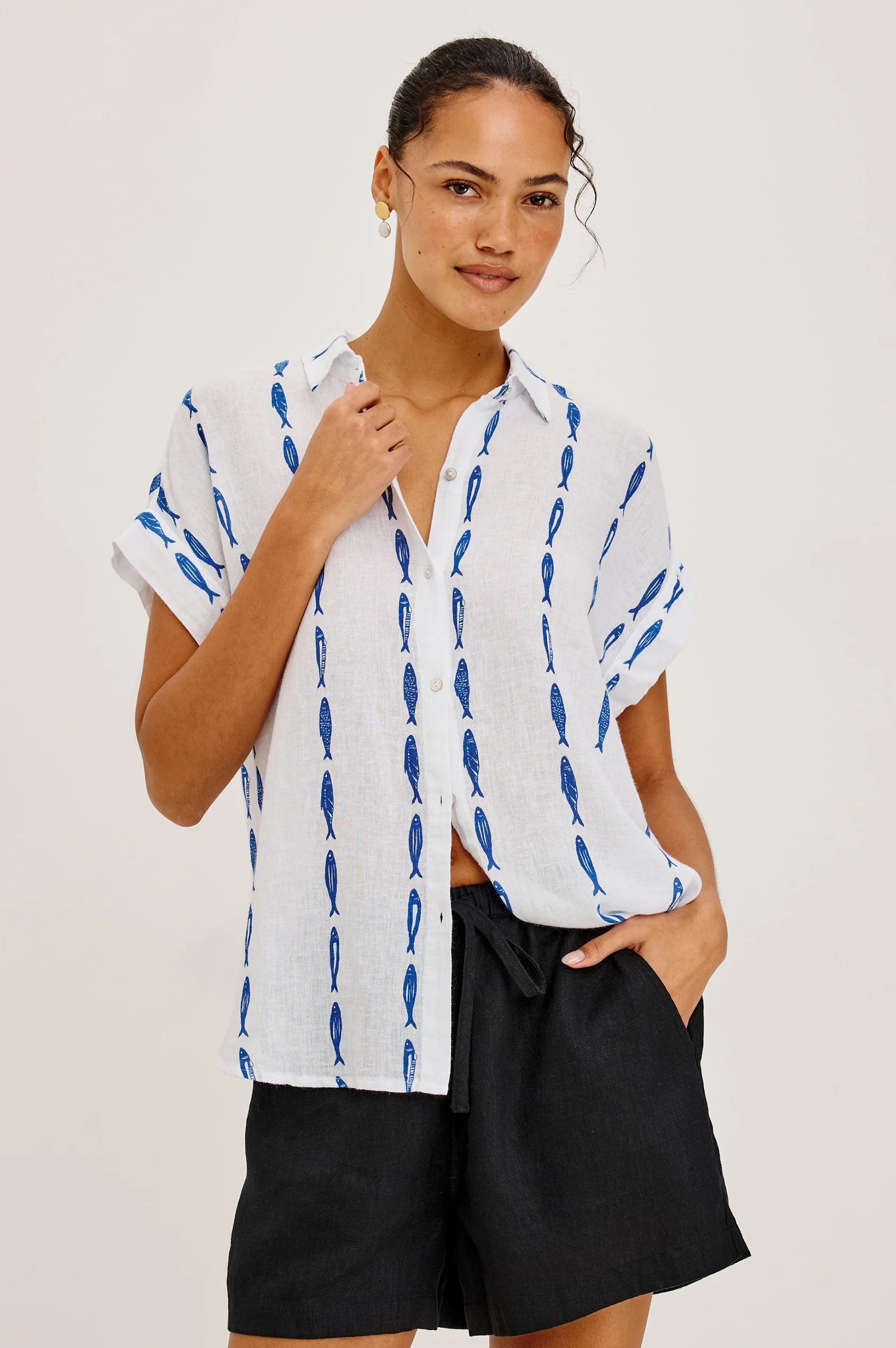 Woman wearing a white shirt with blue patterns and black shorts on a plain background