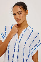 Woman wearing a white shirt with blue fish pattern against a plain background