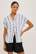 Woman wearing a white shirt with blue patterns and black shorts on a plain background