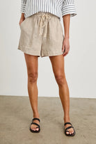 Person wearing beige shorts and black sandals on a plain background