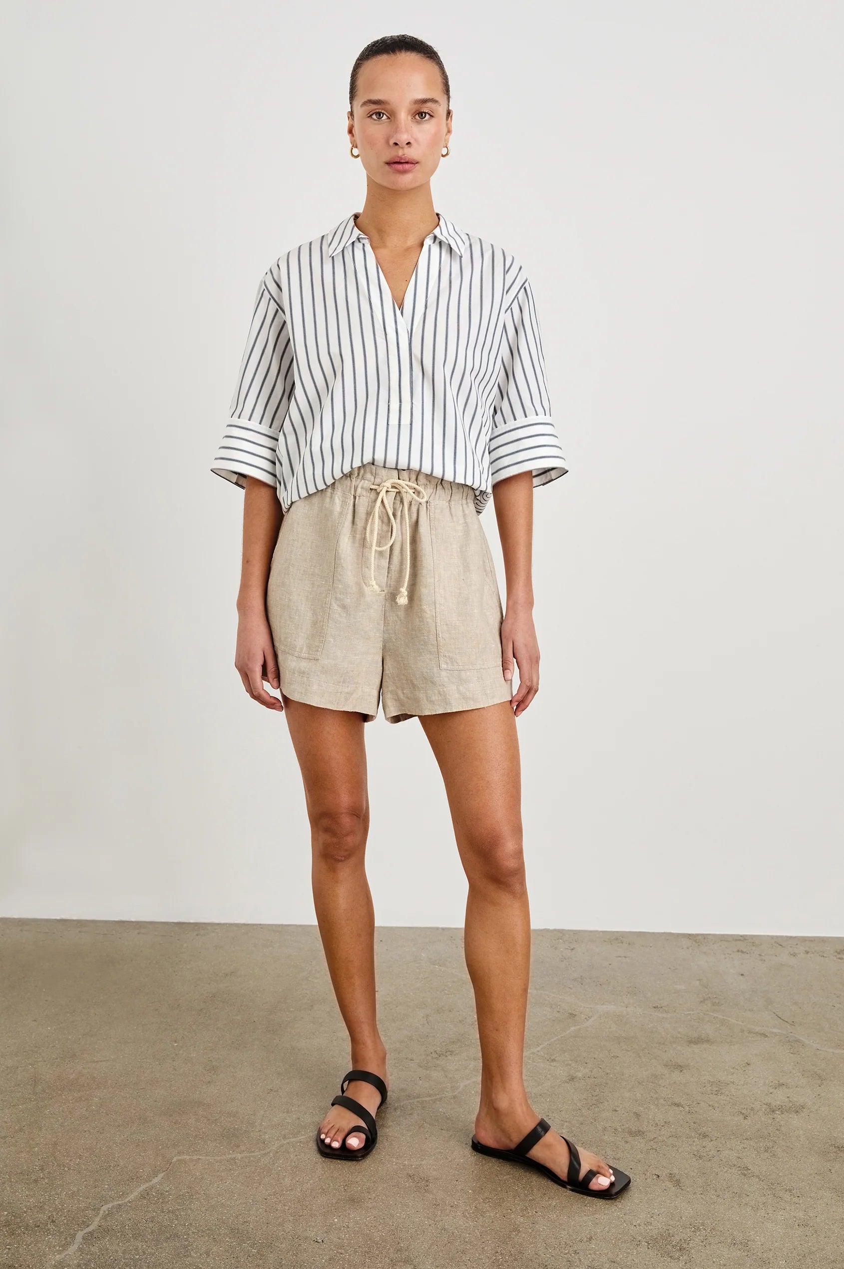 Person wearing a striped shirt and beige shorts on a plain background