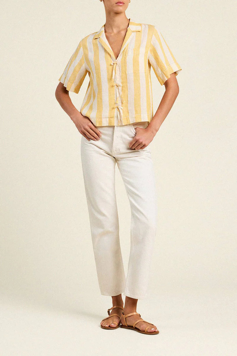 Person wearing a yellow and white striped shirt with white pants on a plain background