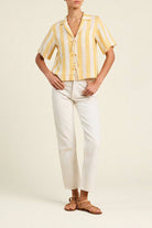 Person wearing a yellow and white striped shirt with white pants on a plain background