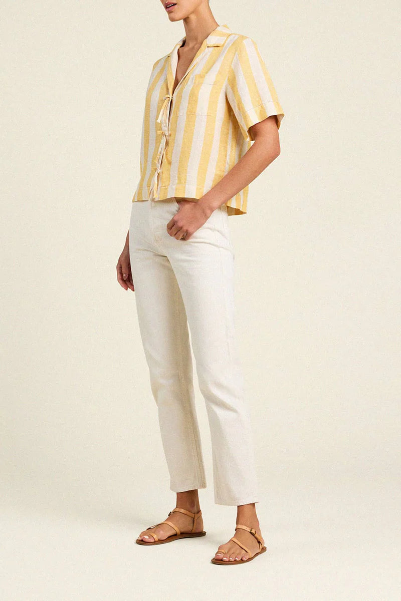 Person wearing a yellow and white striped shirt with white pants on a beige background