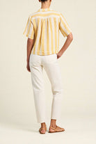 Person wearing a yellow striped shirt and white pants on a beige background