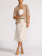 Woman wearing a beige cardigan, white top, and lace skirt on a white background