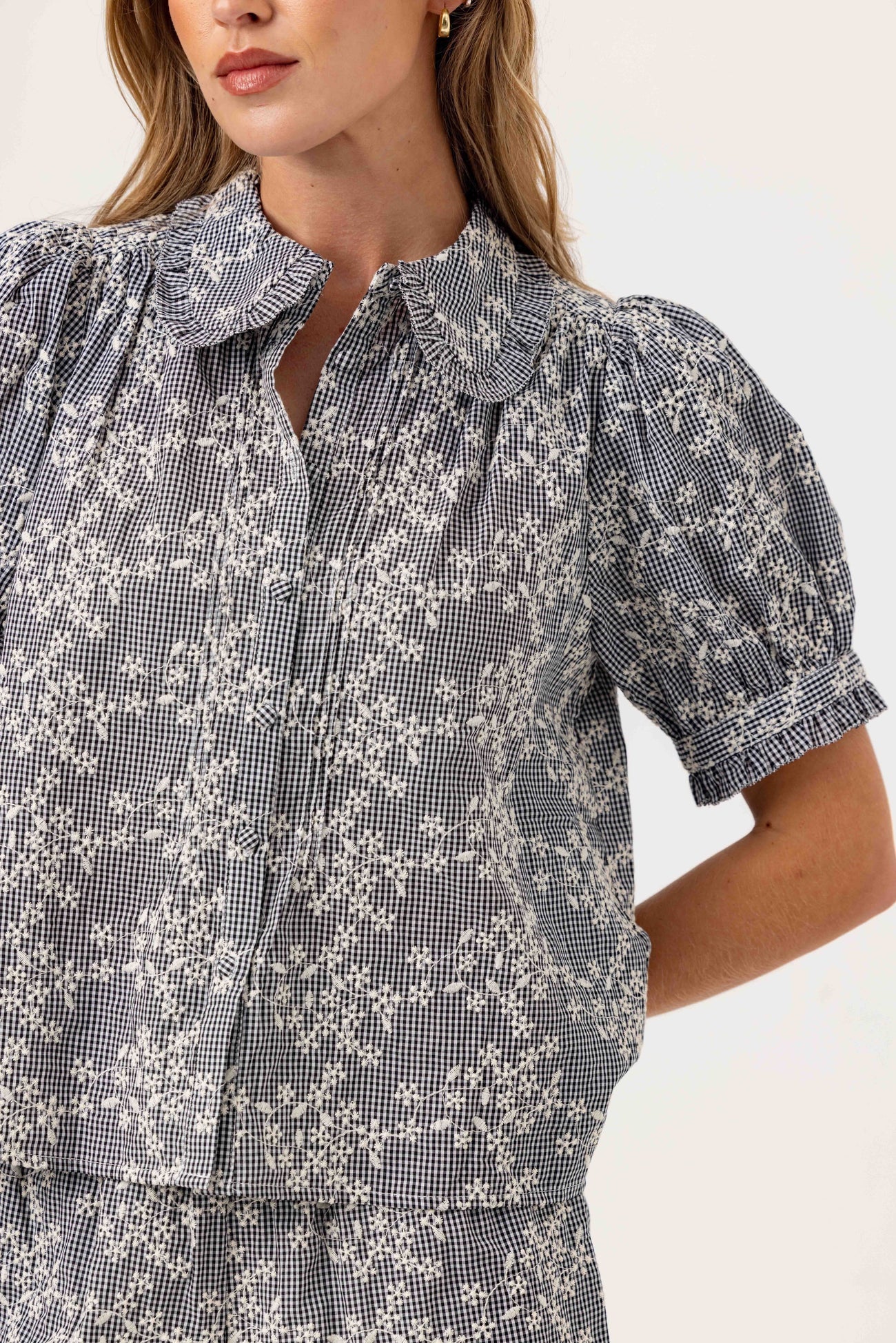 Woman wearing a black and white floral blouse with ruffled collar on a white background