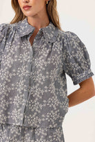Woman wearing a black and white floral blouse with ruffled collar on a white background
