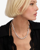 Woman wearing a silver chain necklace against a neutral background