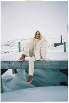 Person sitting on a snowy dock wearing a large white puffer coat.