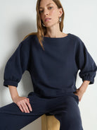Woman wearing a navy blue outfit sitting against a light background