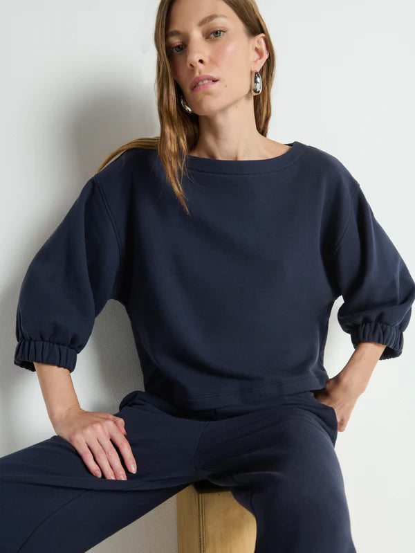 Woman wearing a navy blue outfit sitting against a light background