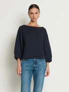 Woman wearing a navy blue top and blue jeans against a plain background