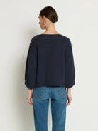 Person wearing a navy sweater and blue jeans against a white background