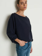 Woman wearing a navy sweater and blue jeans against a white background
