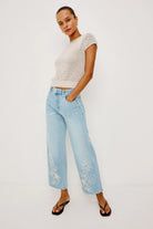 Woman wearing a light-colored top and light blue jeans with floral embroidery on a white background