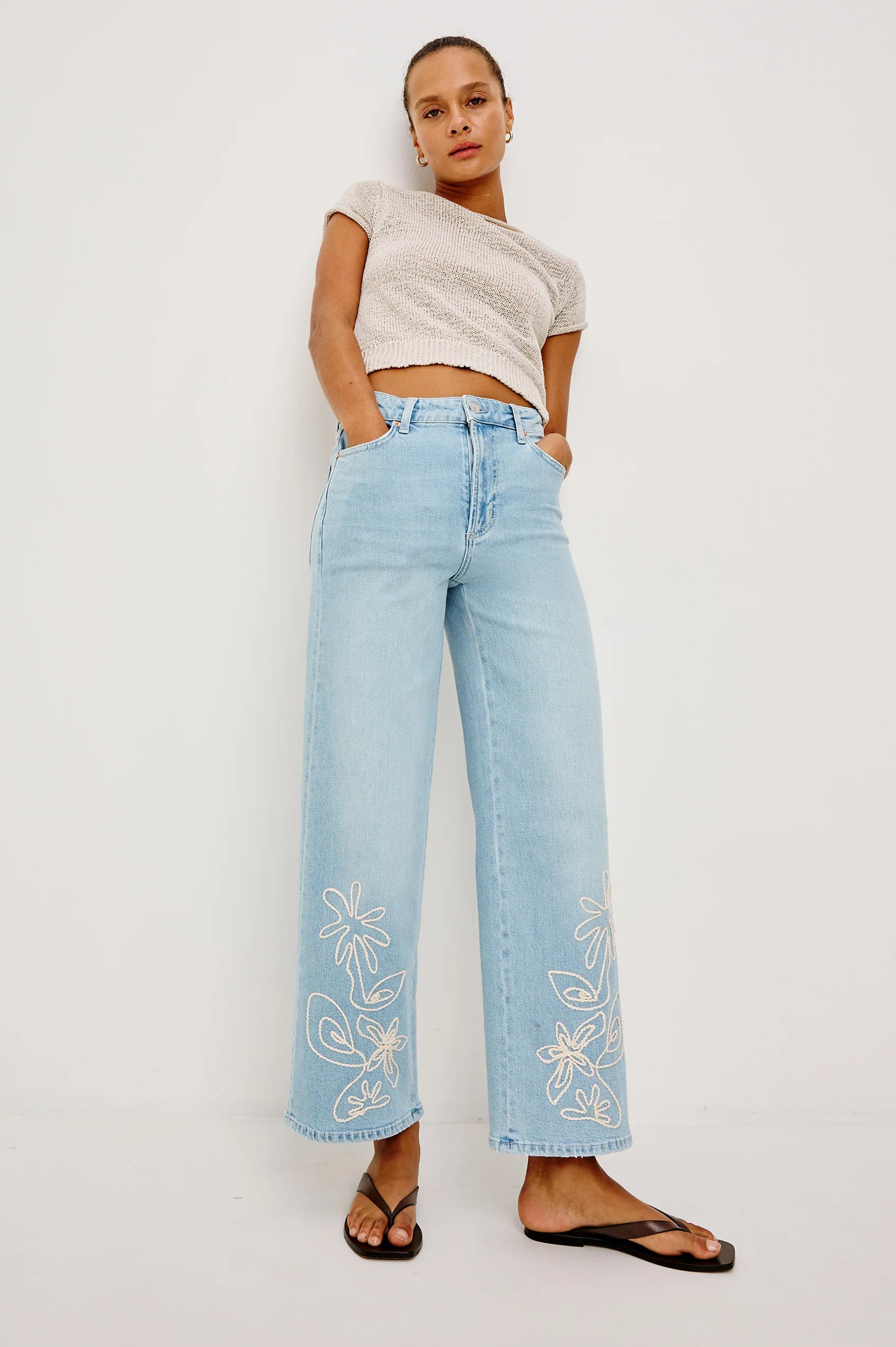Woman wearing light blue jeans with floral embroidery on a white background