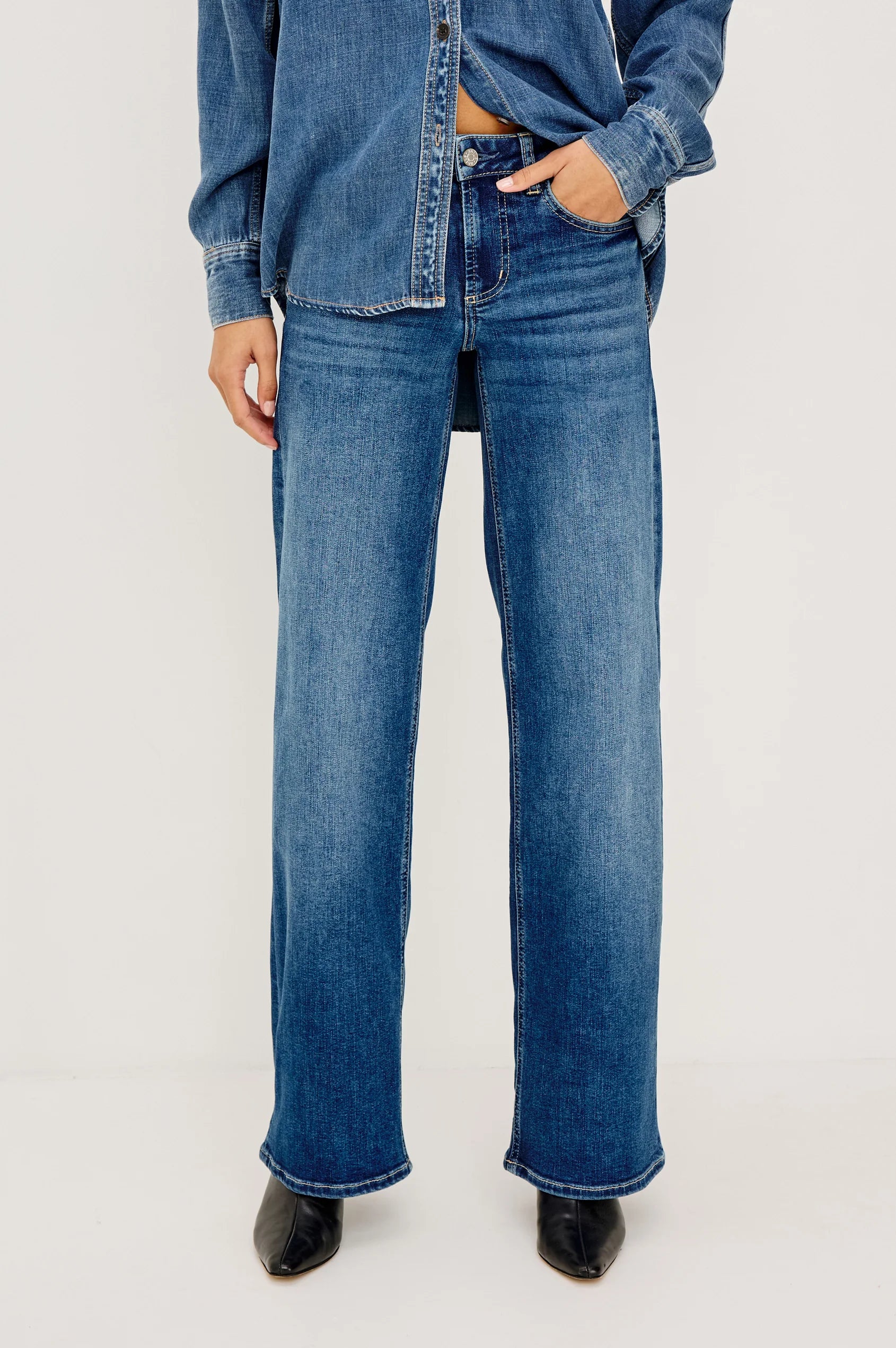 A model wearing a matching blue denim set consisting of a long-sleeve button-up shirt and wide-leg jeans, against a plain white studio background.