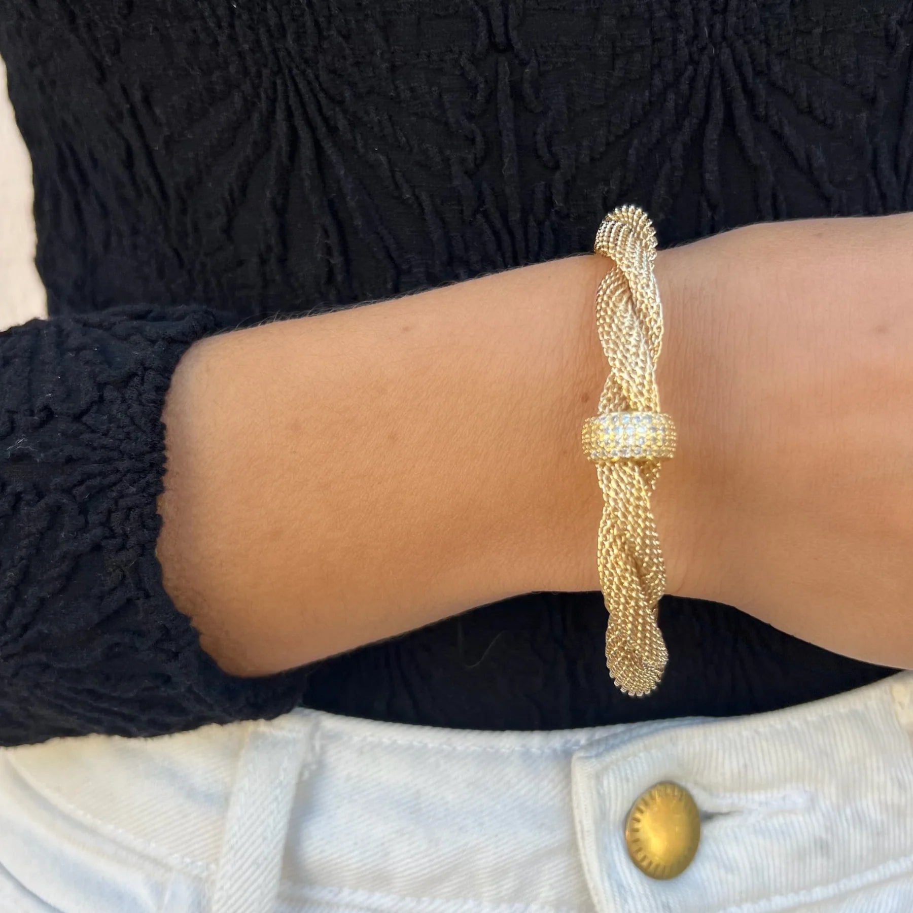 Gold braided bracelet on a wrist with a dark textured background