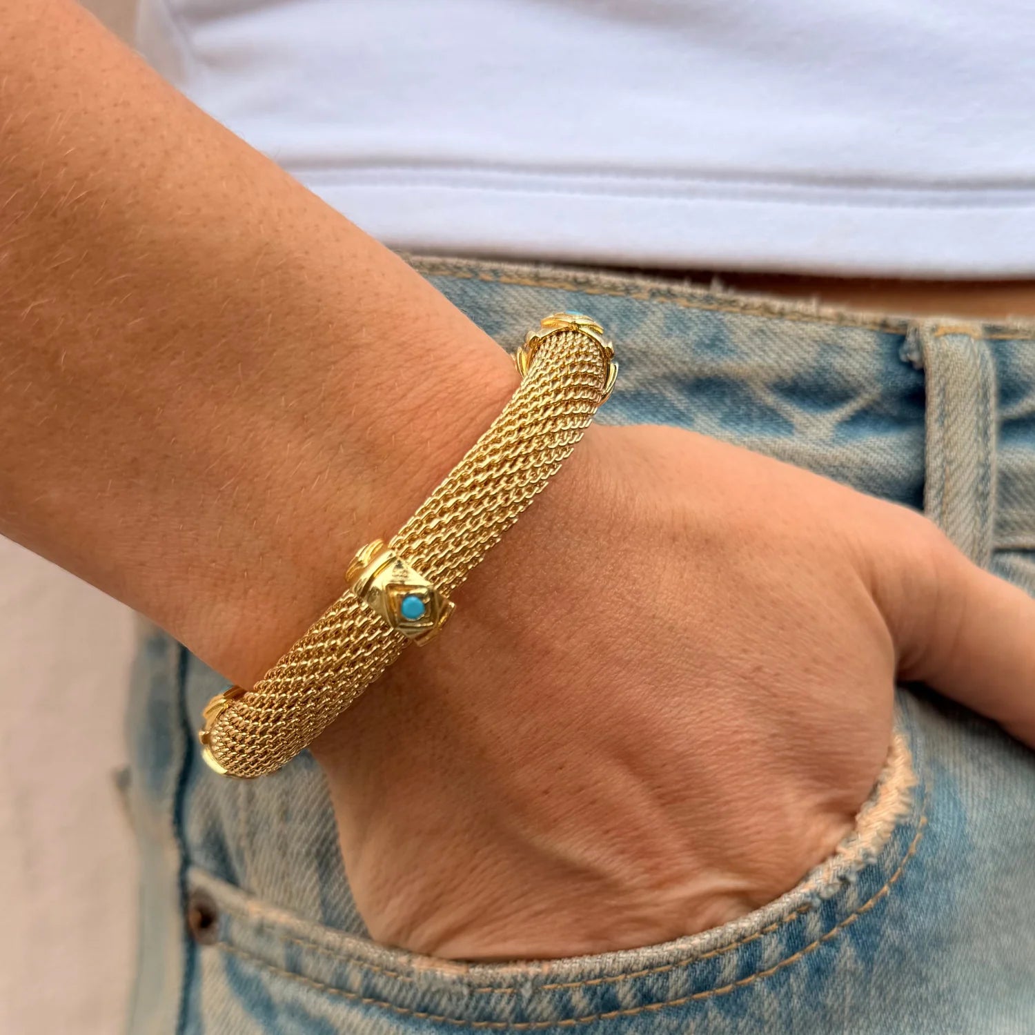 Gold bracelet with a blue gemstone on a wrist, wearing a denim jacket.