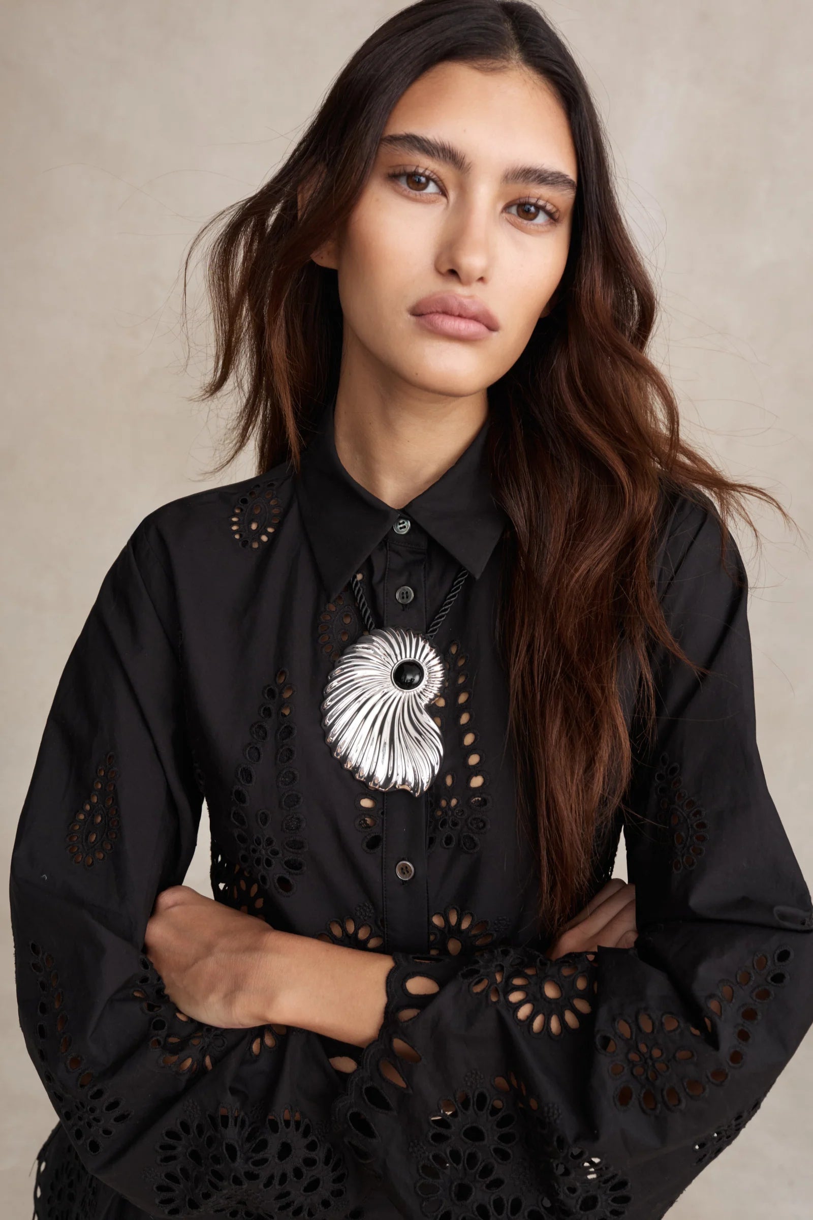 Woman wearing a black blouse with intricate cut-out designs and a decorative brooch.