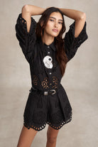 Woman wearing a black outfit with cut-out details on a beige background