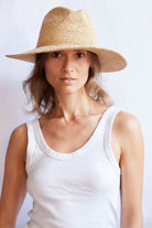Woman wearing a straw hat and white tank top against a light background