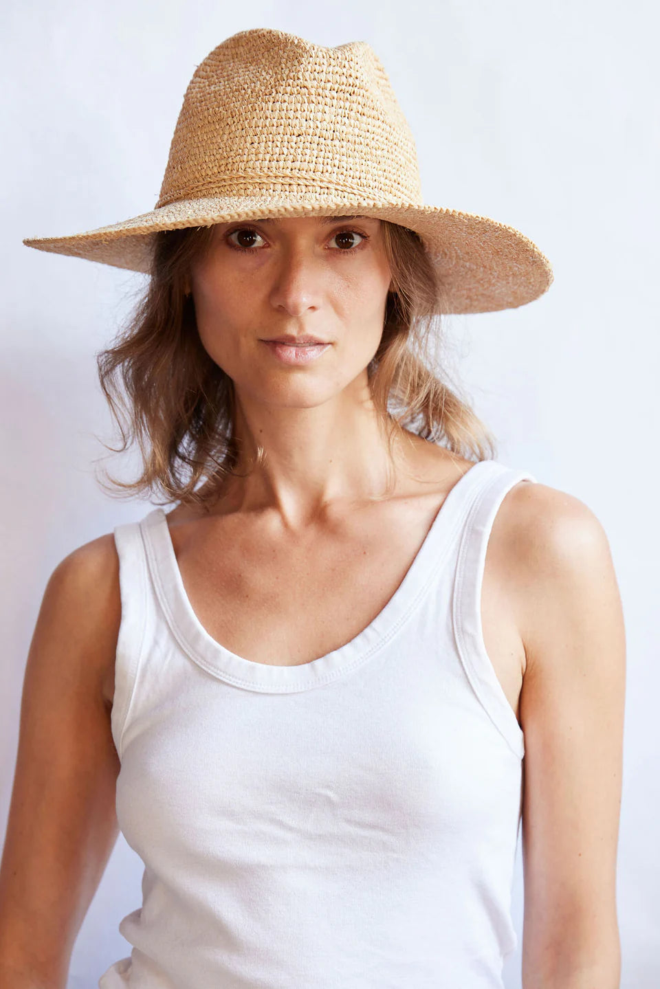 Woman wearing a straw hat and white tank top against a light background