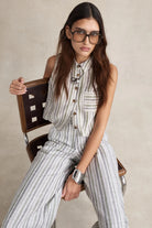 Woman wearing a striped outfit sitting on a chair against a neutral background