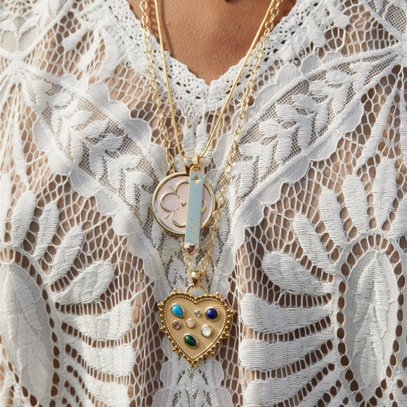 Close-up of a person wearing a gold necklace with a heart-shaped pendant on a lace garment.