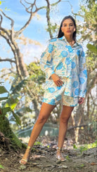 Woman in a floral dress standing in a natural setting with trees and greenery.