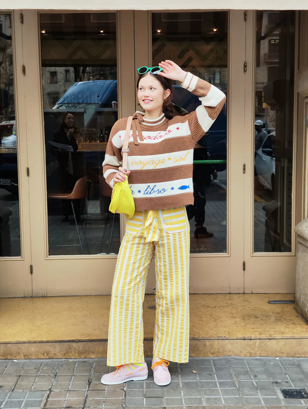 Woman in a striped sweater and yellow pants standing on a street.