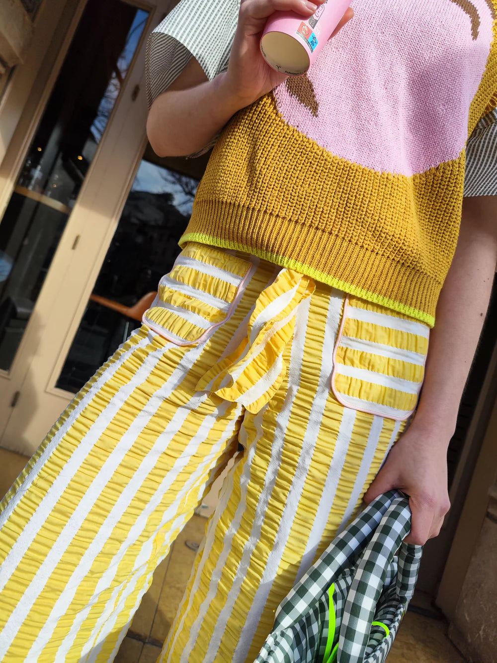 Person wearing a yellow and pink top with yellow and white striped pants, holding a pink bottle.
