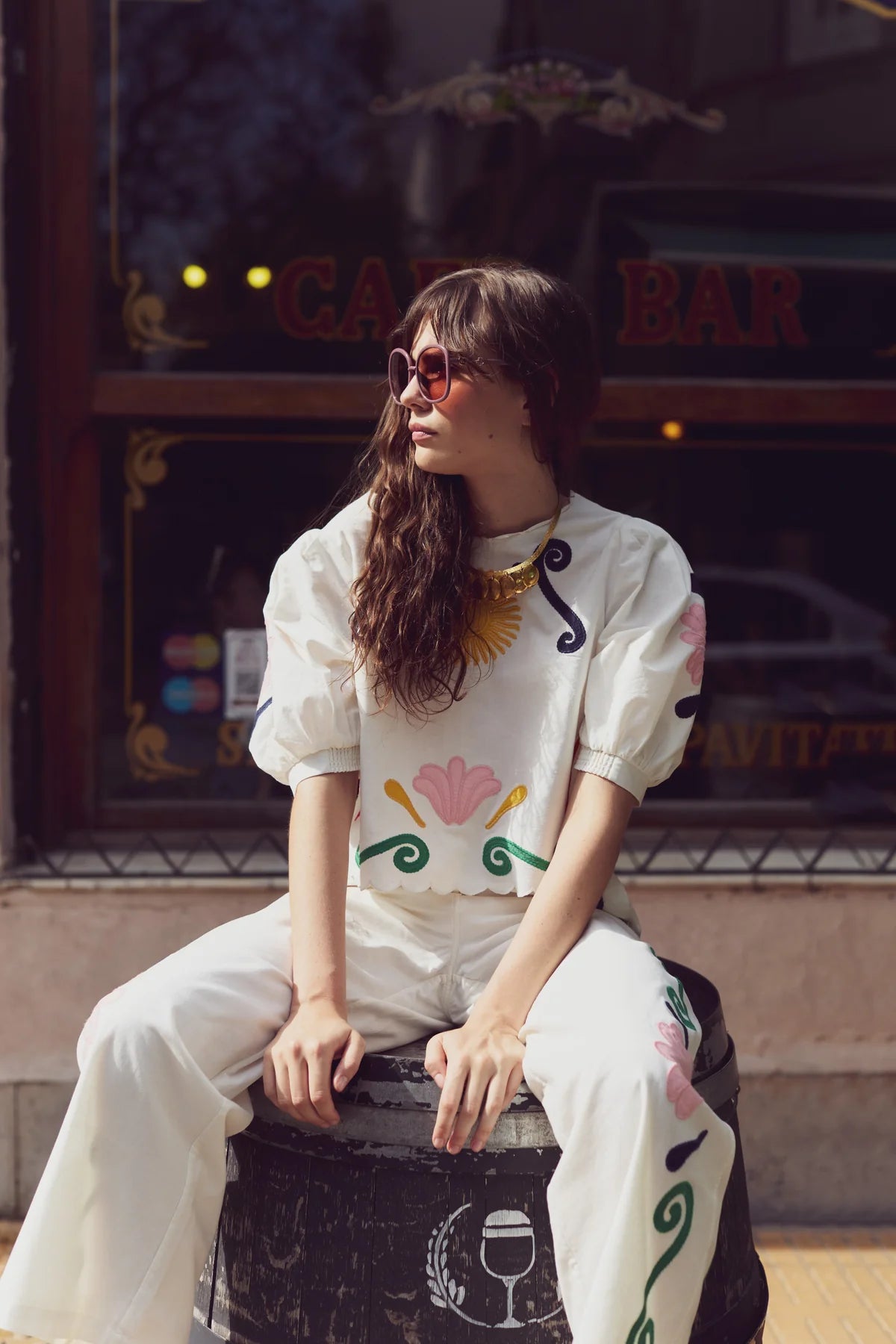 Woman sitting on a barrel in front of a bar with decorative elements.