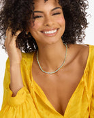 Woman wearing a yellow dress with a deep neckline, smiling and touching her hair.