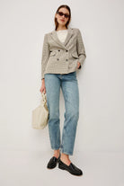 Woman wearing a checkered blazer, white shirt, blue jeans, and black shoes on a plain background