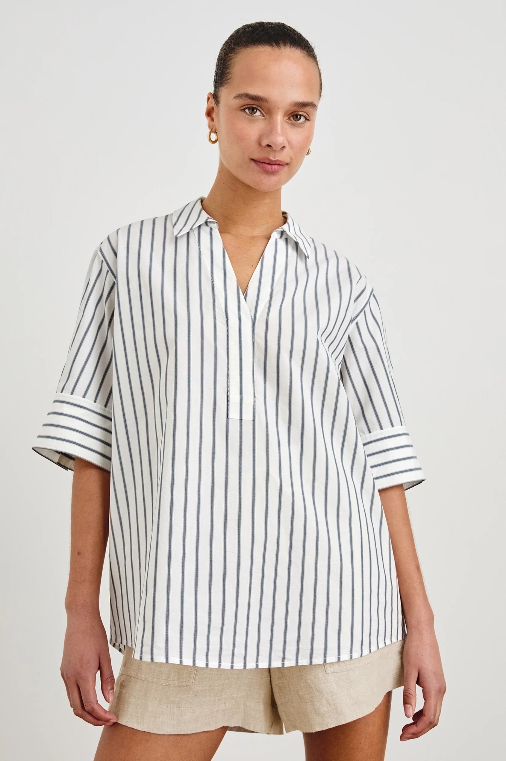 Woman wearing a striped shirt and beige shorts on a plain background