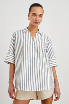 Woman wearing a striped shirt and beige shorts on a plain background