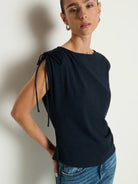 Woman wearing a black sleeveless top with tie details against a neutral background