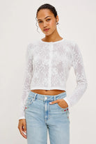 Woman wearing a white lace top and light blue jeans on a white background