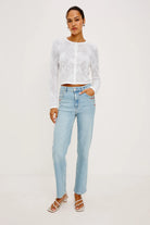 Woman wearing a white lace top and light blue jeans on a white background