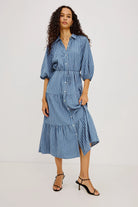 A woman modeling a blue and white vertically striped midi dress with puff sleeves and a tiered skirt, shown from a full body front angle against a plain white studio background.