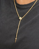 Gold lariat necklace with a green gemstone on a black background